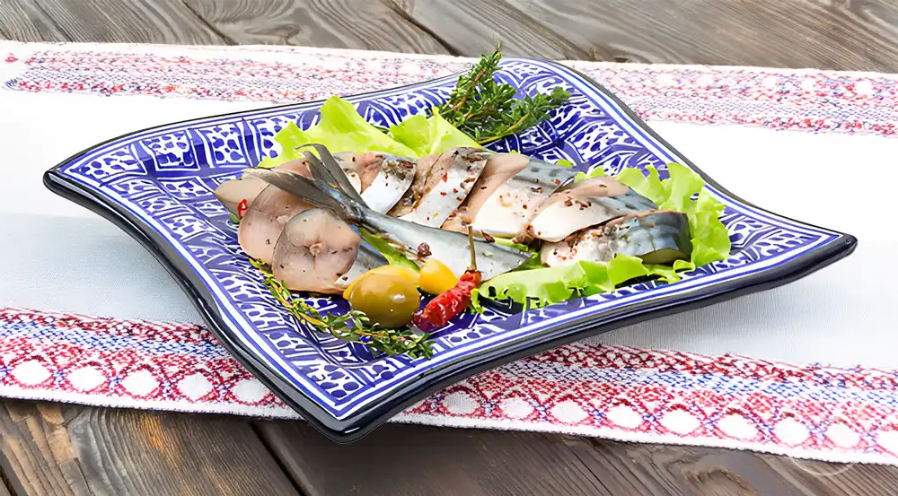 Порізані шматочки маринованої скумбрії, перекладені кільцями цибулі у скляному посуді.