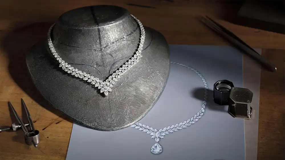 Inside Harry Winston: Valentyna Zhytnyk on Luxury Jewelry, Professional Ambitions, and the Future of High Jewelry MODISTA A luxury diamond necklace on a display stand next to a hand-drawn jewelry sketch, professional gemologist loupe, and design tools on a wooden workshop table.